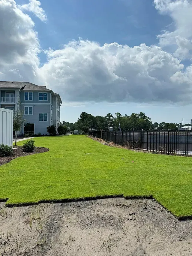 A large lawn with a fence and a building in the background.