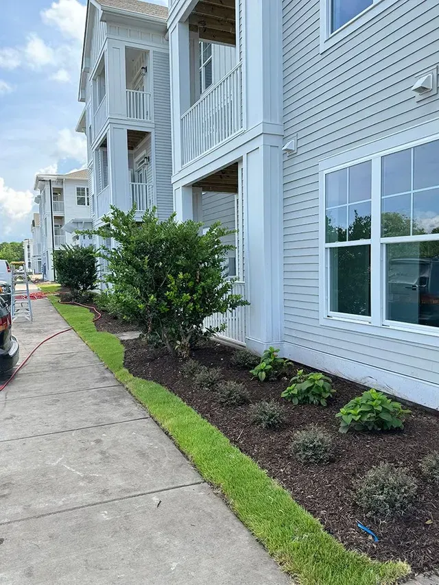 A white apartment building with a lot of windows and bushes in front of it.