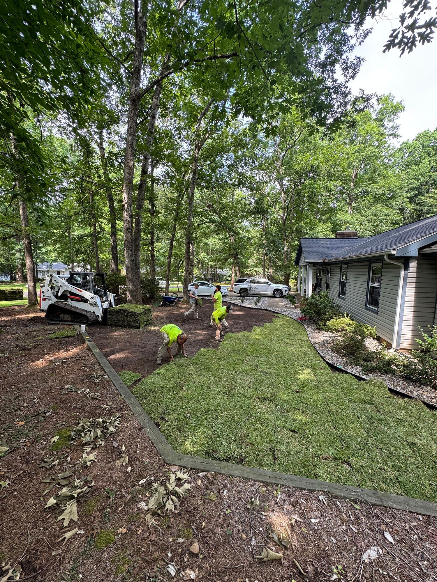 A group of people are working on a lawn in front of a house.