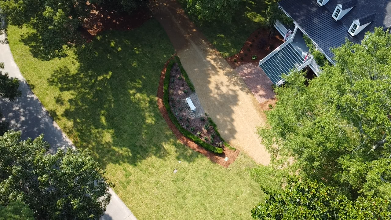 An aerial view of a house and a driveway surrounded by trees.