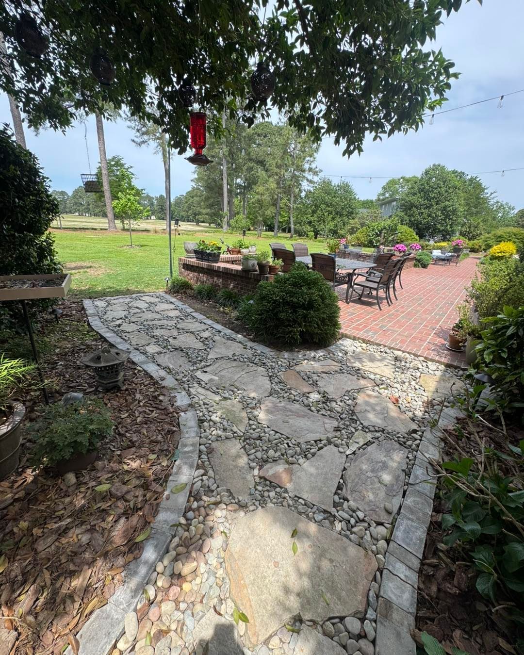 A stone walkway leading to a patio with a bird feeder hanging from a tree.