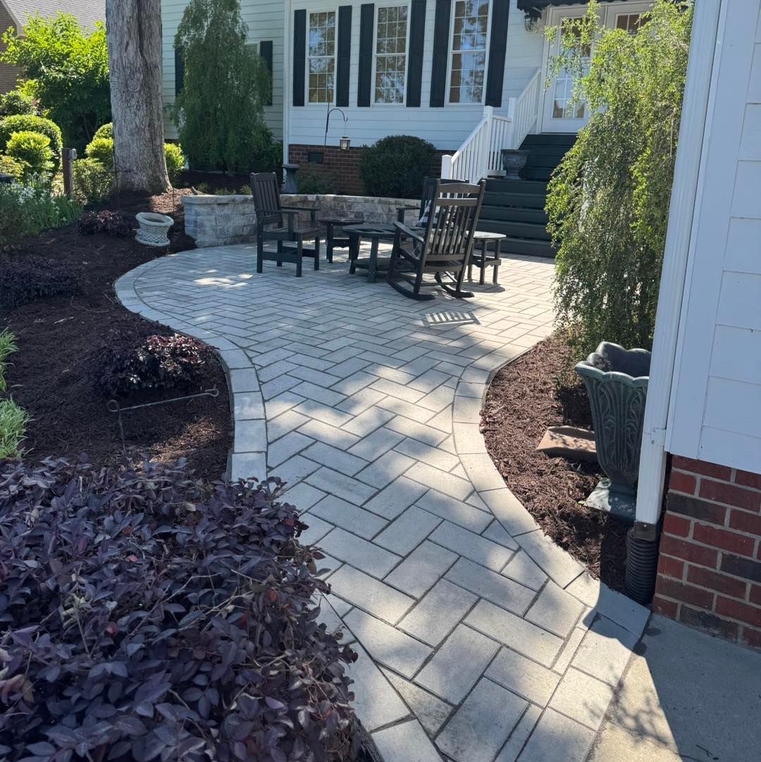 A brick walkway leading to a patio with rocking chairs