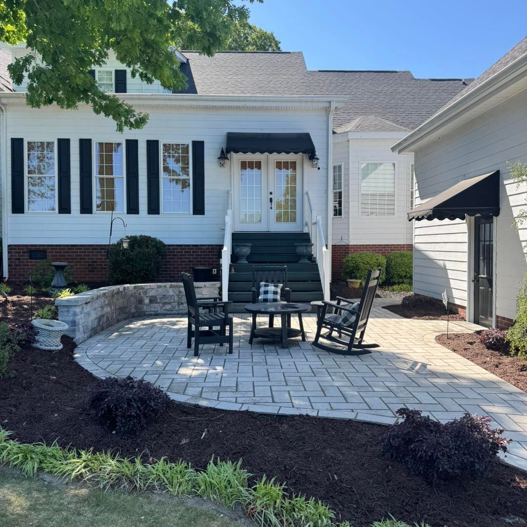 There is a patio in front of a house with rocking chairs and a table.