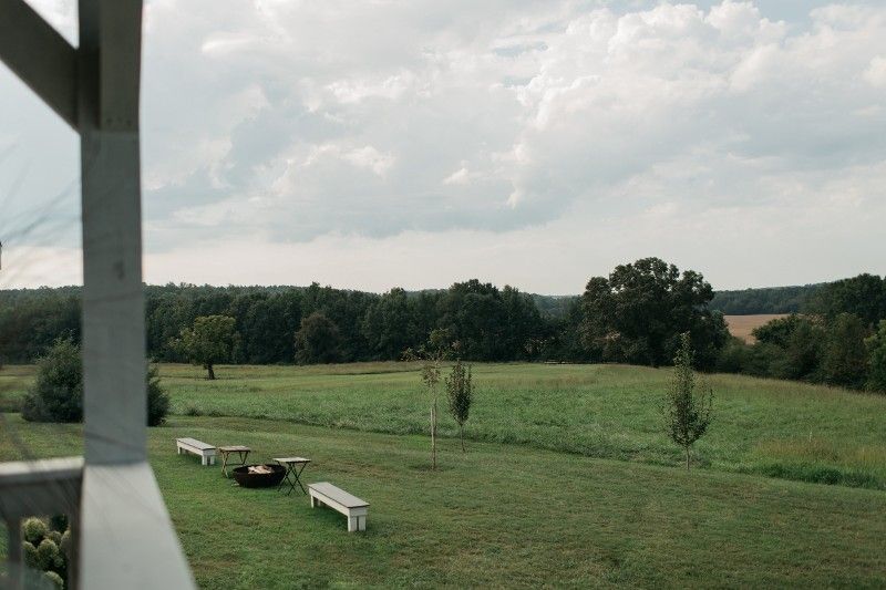 A view of a field from a porch with benches and a fire pit.