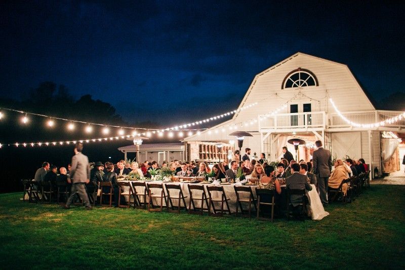 A large group of people are sitting at tables in front of a barn at night.