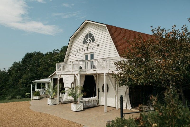 A large white barn with a balcony and trees in front of it.