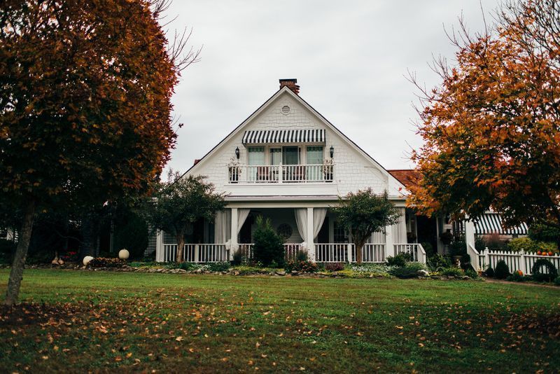 A large white house with a porch and trees in front of it.
