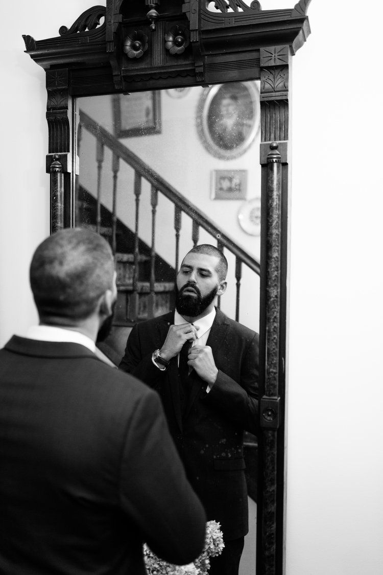 A man in a suit is adjusting his tie in front of a mirror