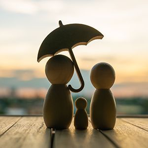 a family of wooden dolls holding an umbrella on a wooden table .