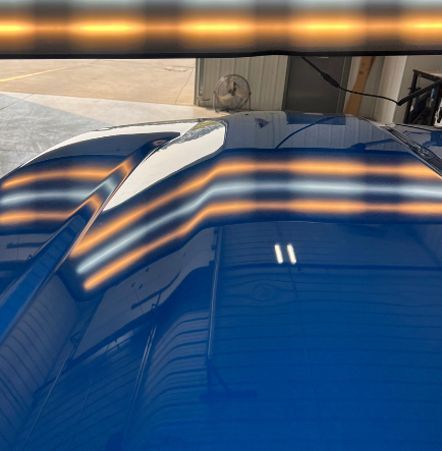 A close up of a blue car hood with dents in it.