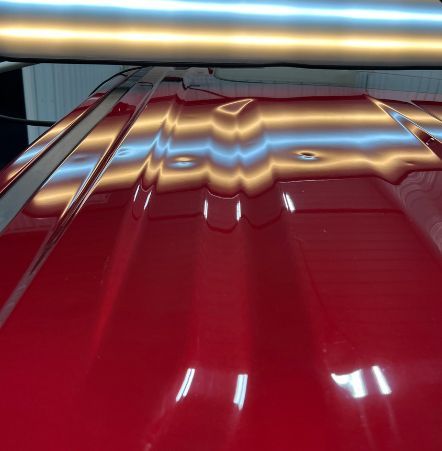 A close up of a red car hood with dents on it.