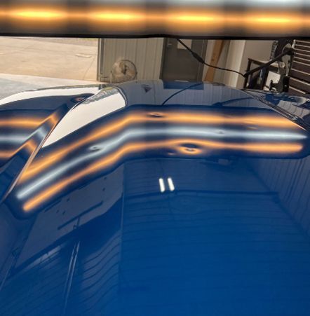 A close up of a blue car with dents on the hood