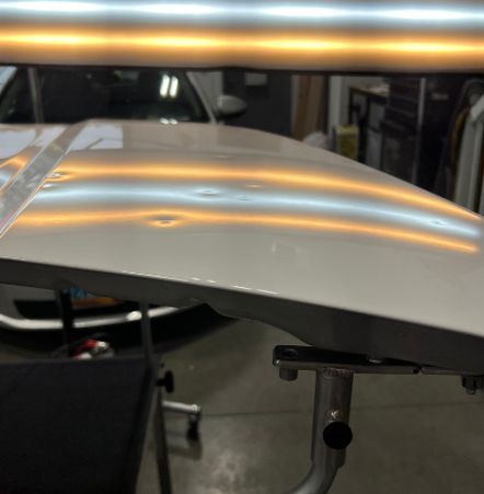 A close up of a car hood with dents on it.