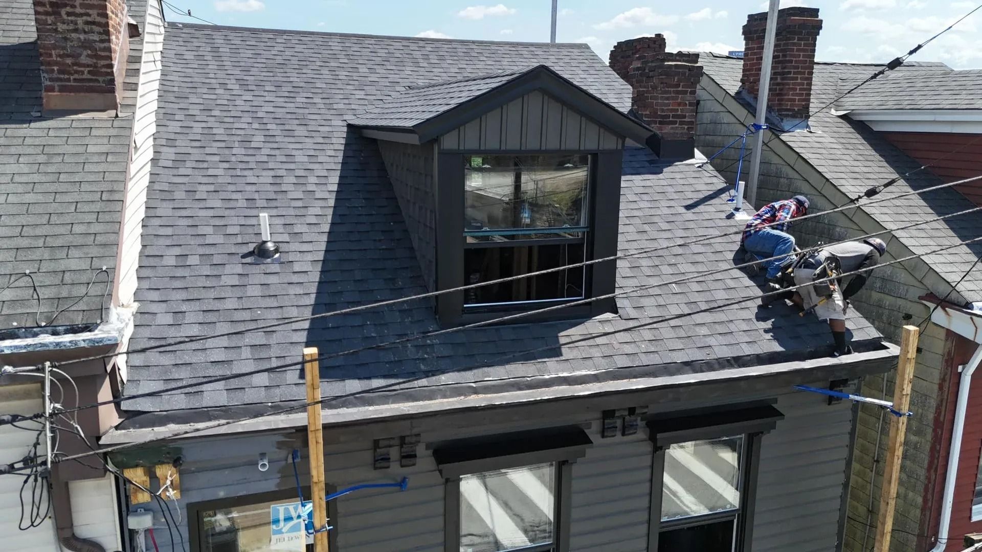 A person on a roof working on a house with a dark gray exterior and a dormer window.