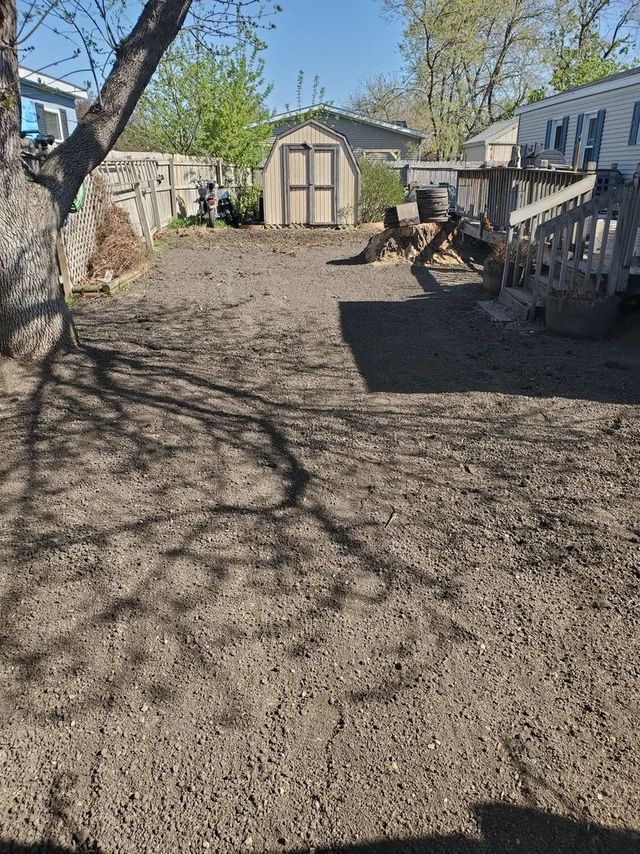 Backyard with a small shed and patchy brown ground. A tree casts a shadow on the yard.