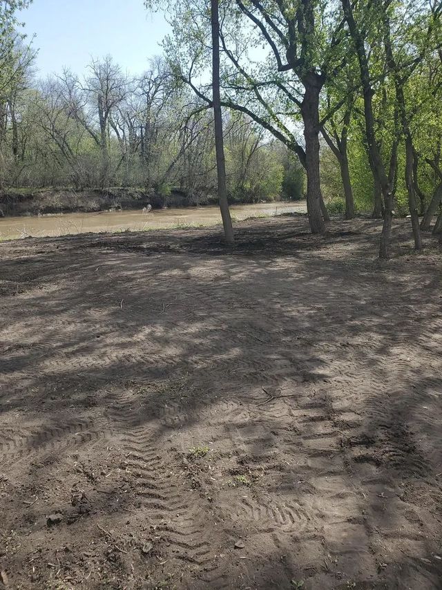 Dirt clearing in a wooded area; shadows, tire tracks visible, trees in the background, blue sky.
