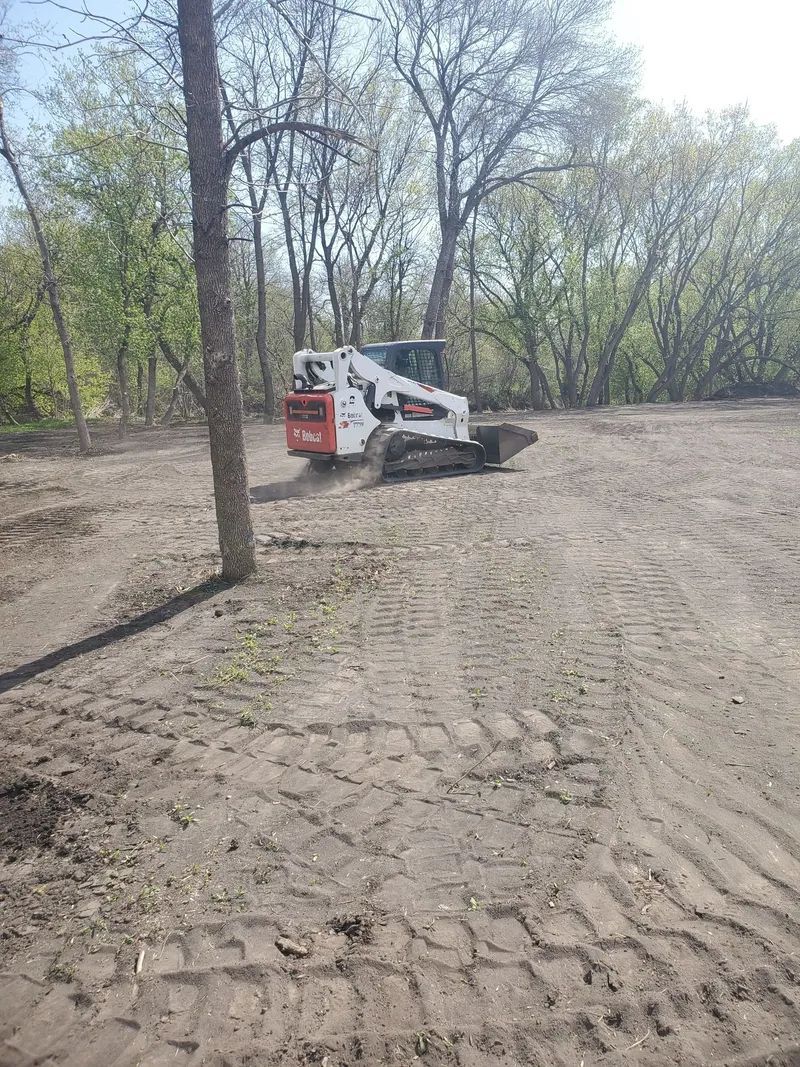 Bobcat skid-steer loader on dirt clearing area, trees in background, sunny day.
