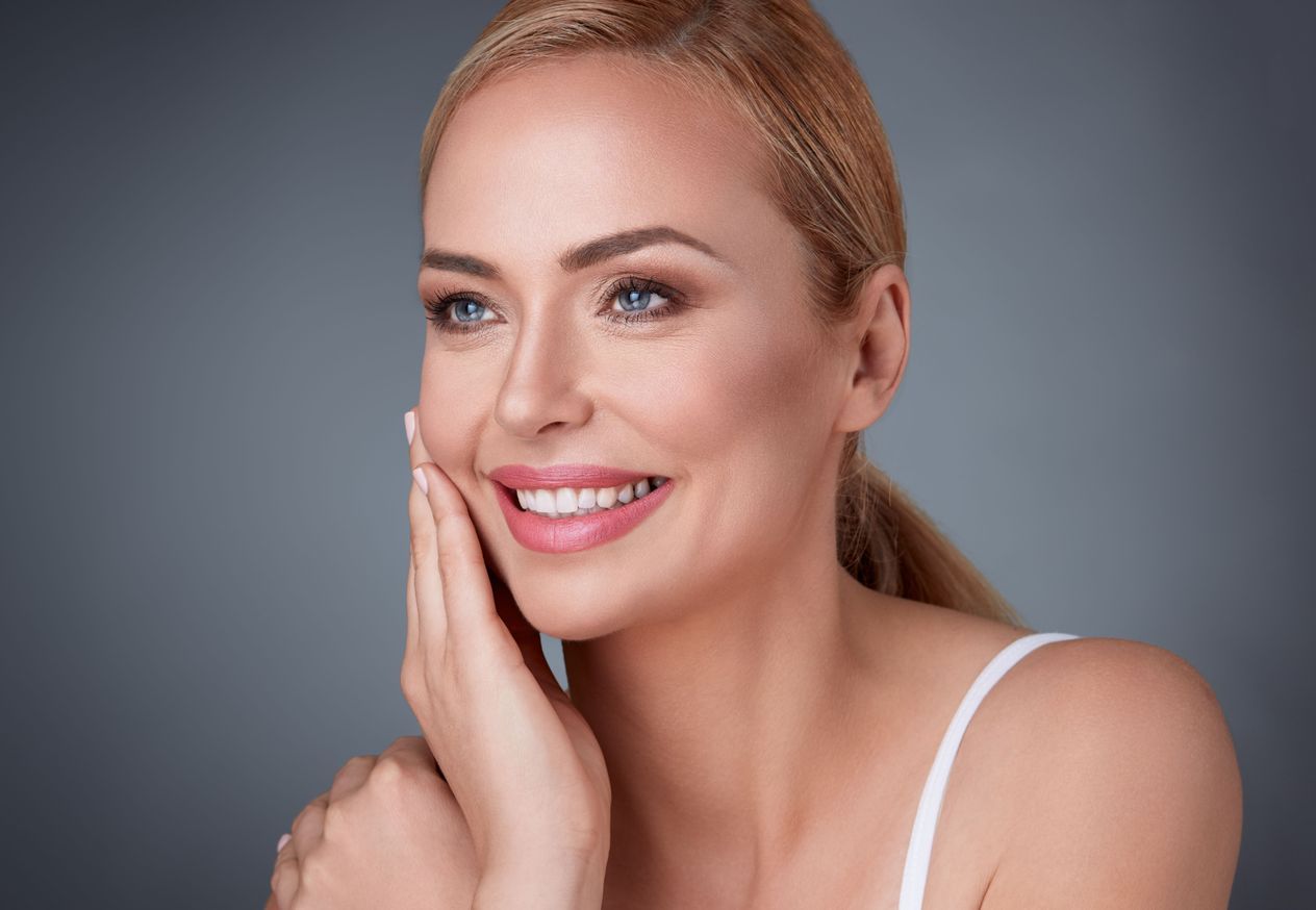 A woman is touching her face with her hand and smiling.