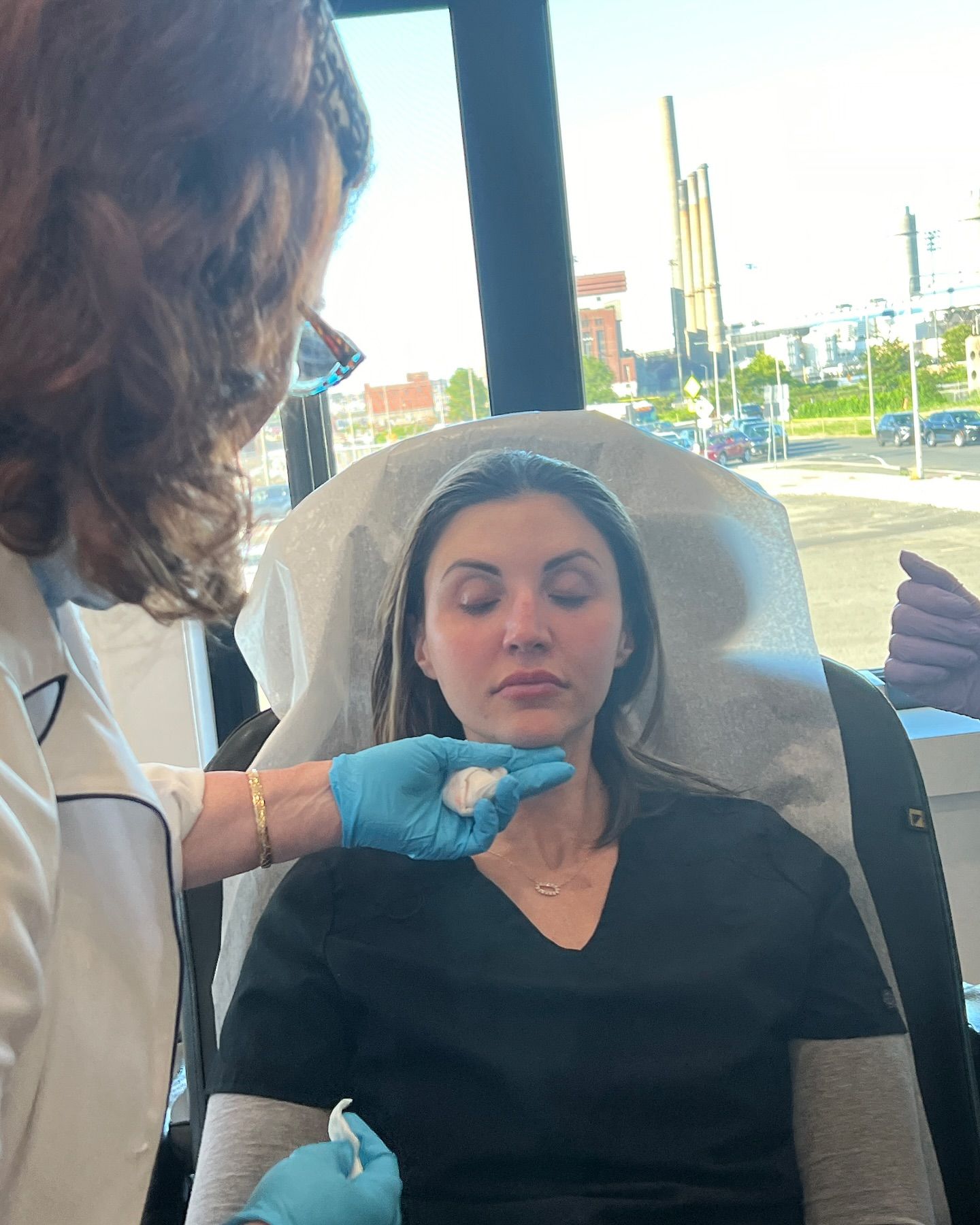A woman is getting a facial treatment from a doctor while sitting in a chair.