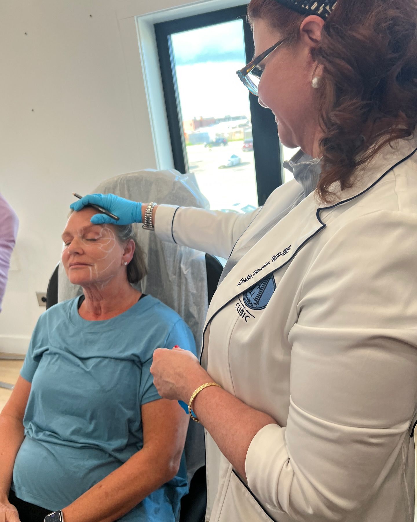 A woman is sitting in a chair while a doctor examines her face.