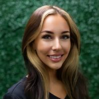 A woman with long hair is smiling in front of a green wall.