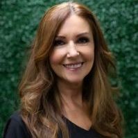 A woman with long brown hair is smiling in front of a green wall.