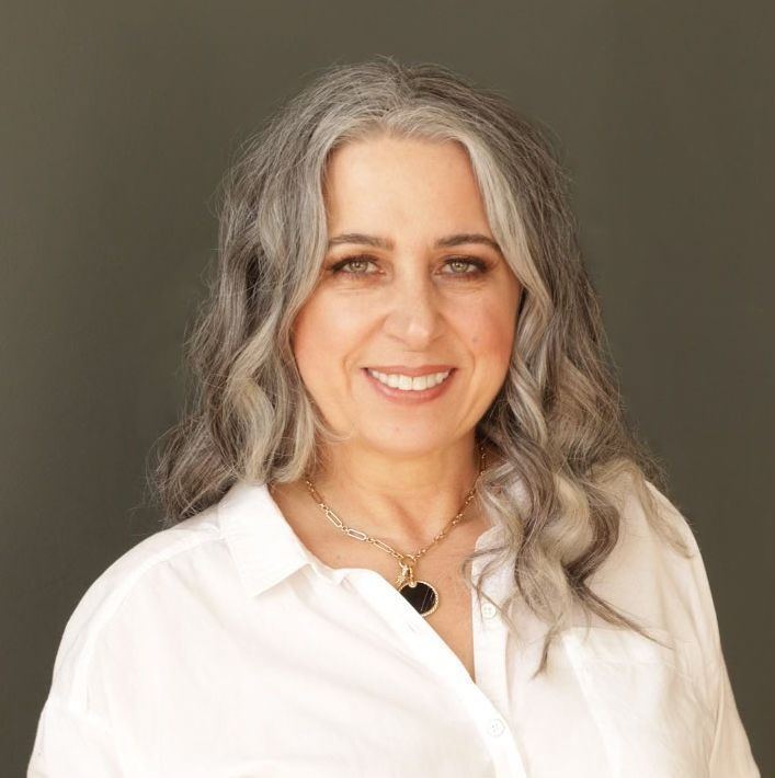 A woman with gray hair is wearing a white shirt and a necklace.