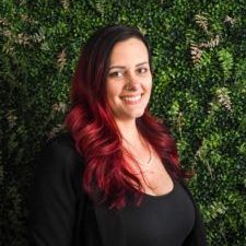 A woman with red hair is smiling in front of a green wall.