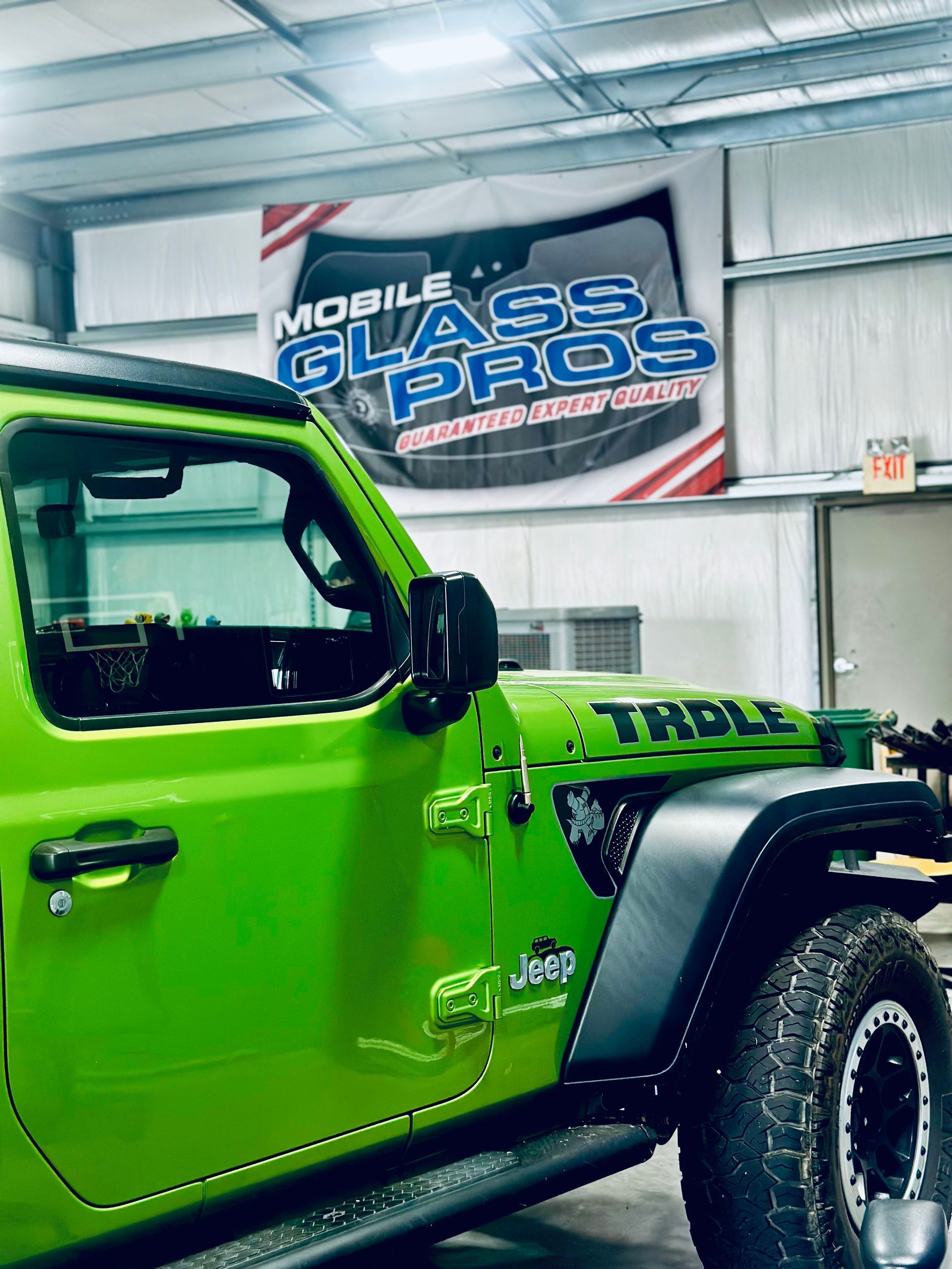 Green Jeep in a garage with "Mobile Glass Pros" banner.