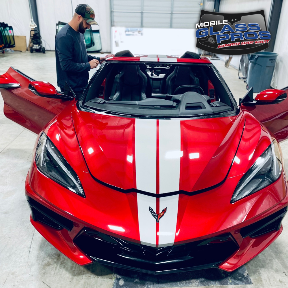 Red Corvette convertible with white racing stripes, doors open, being worked on by a person.