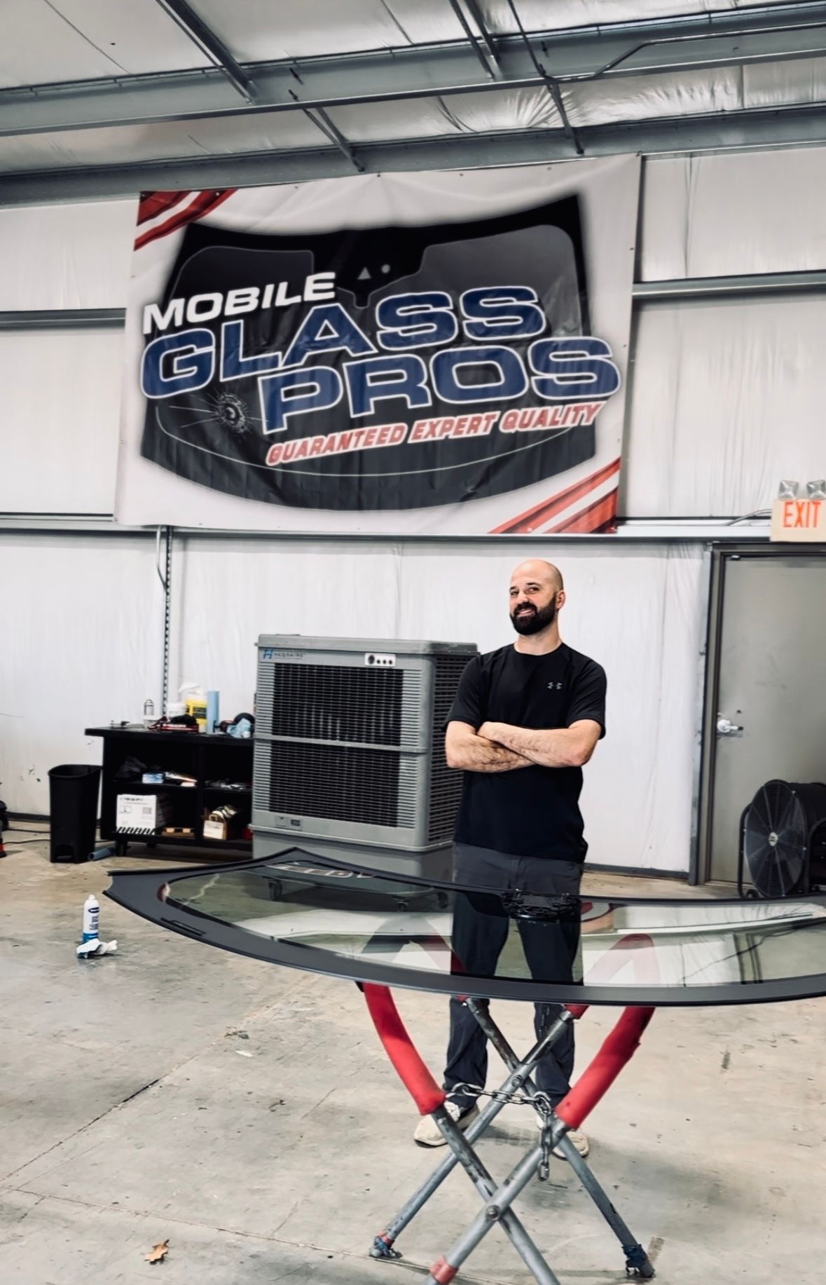 Man standing in a shop, arms crossed, in front of a windshield and a 