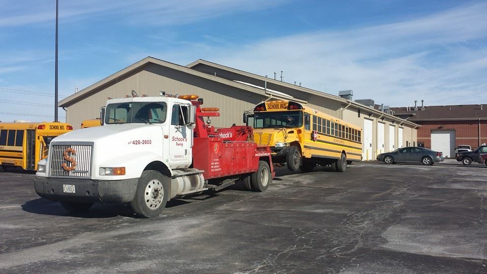 A tow truck is towing a school bus in a parking lot.