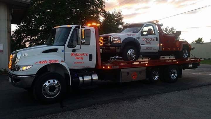 A tow truck with two cars on the back of it.