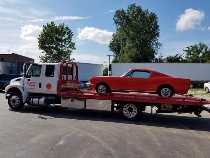 A red mustang is being towed by a tow truck.
