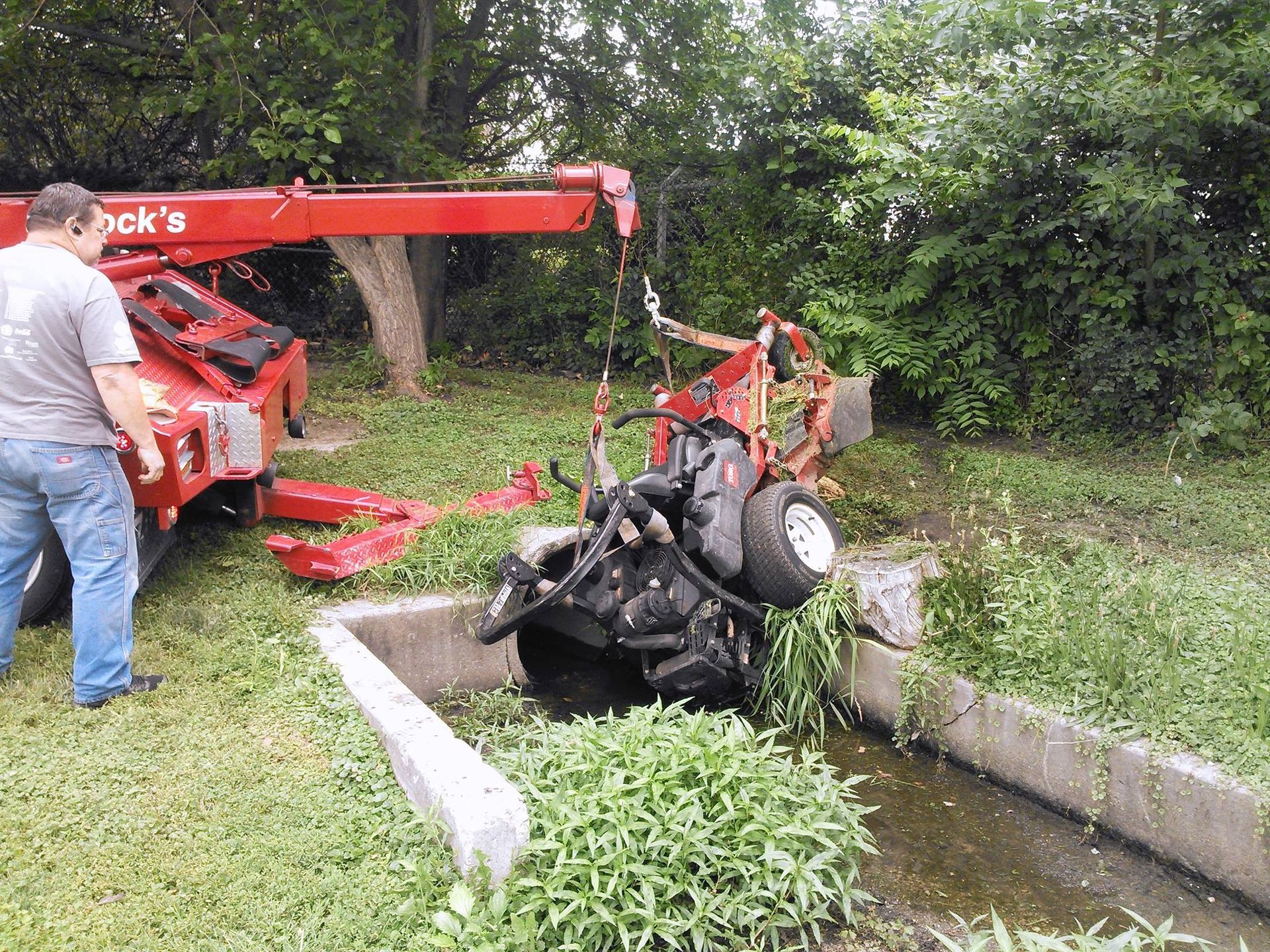 A man is standing next to a hook crane that is lifting a vehicle.
