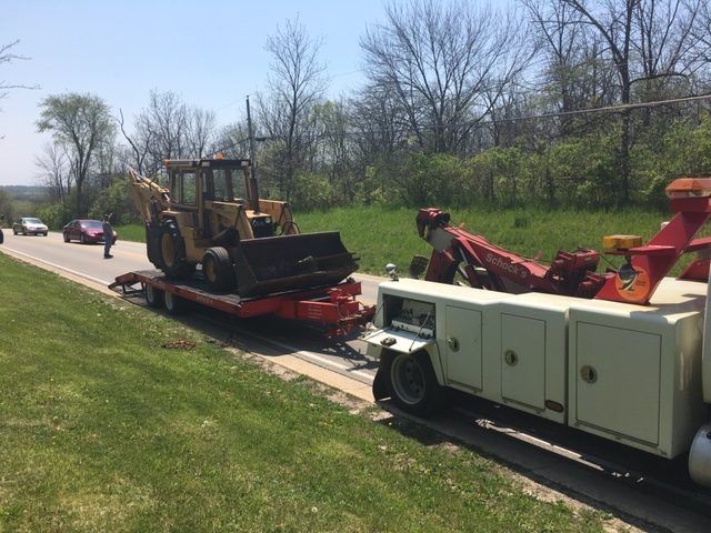 A tow truck is carrying a tractor on a trailer.