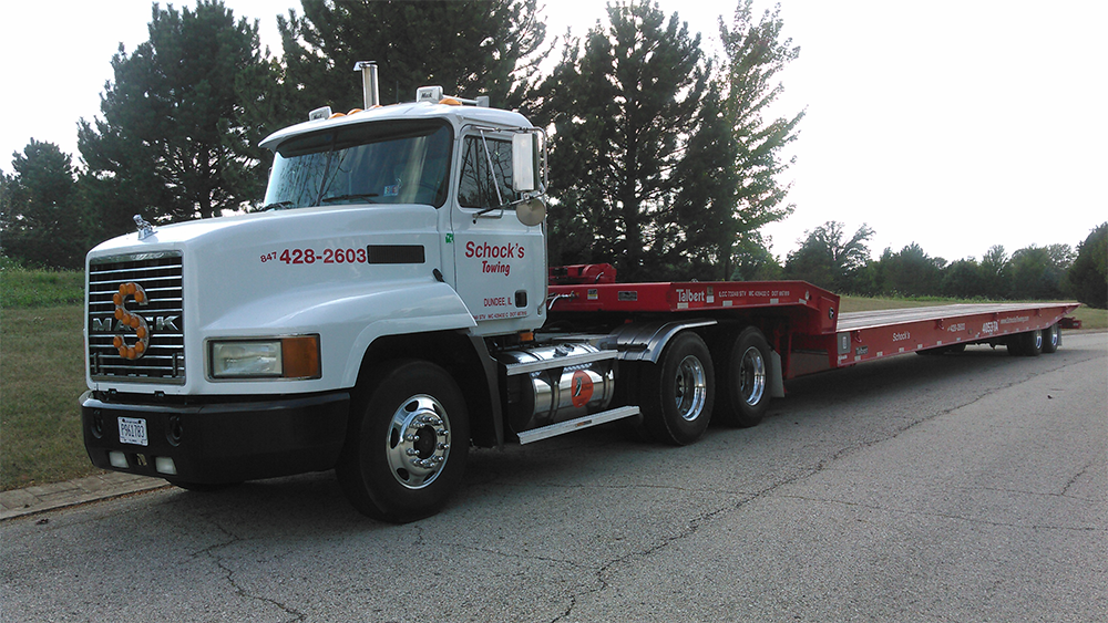 A Schock's Towing semi truck with a flatbed trailer is parked on the side of the road.