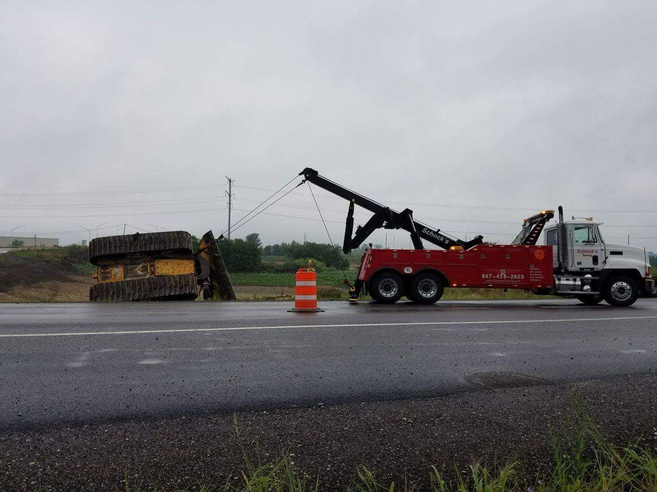 A tow truck is towing a bulldozer on the side of the road.