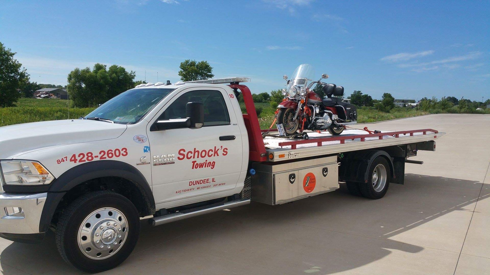 A tow truck with a motorcycle on the back is parked on the side of the road.