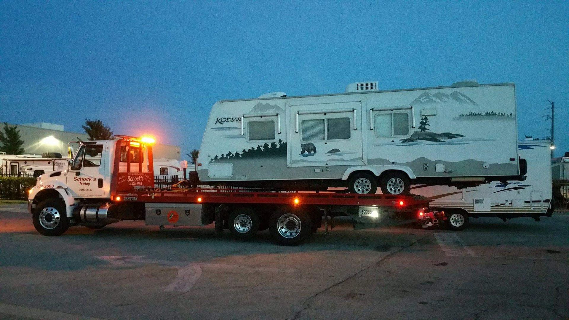 A tow truck is carrying a RV on a trailer.