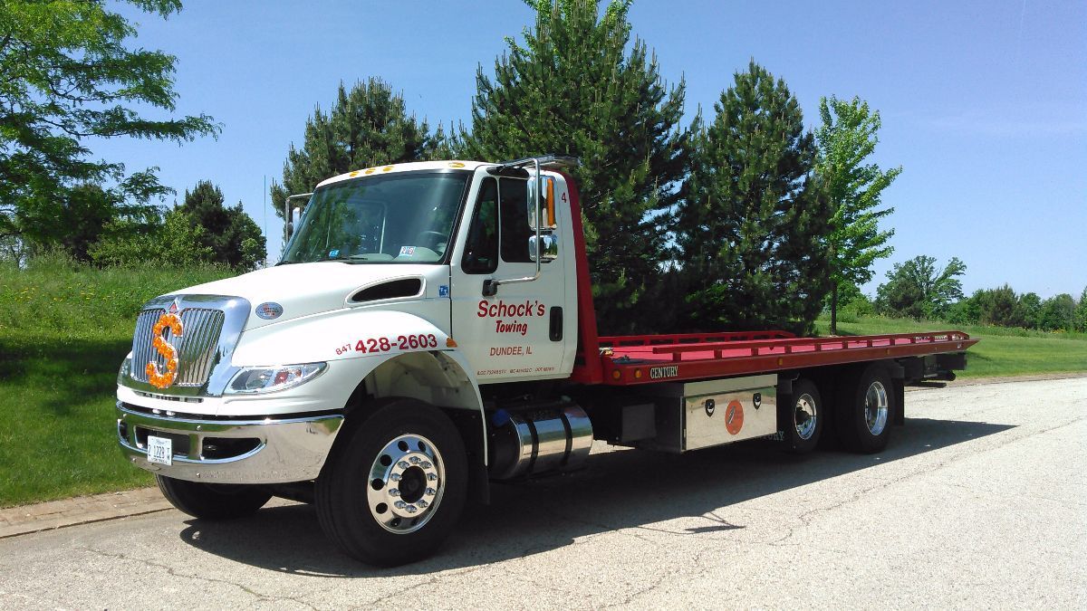 A white tow truck with a red bed is parked on the side of the road.