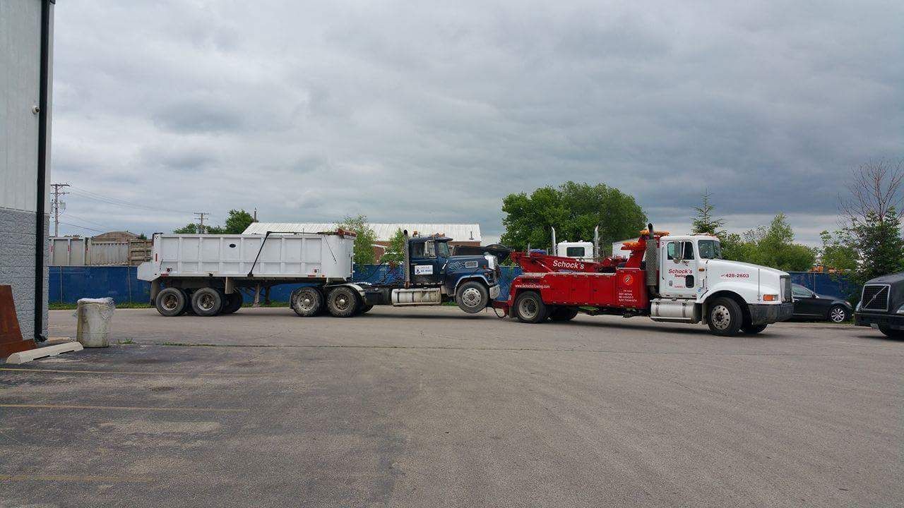 A tow truck is towing a dump truck in a parking lot.