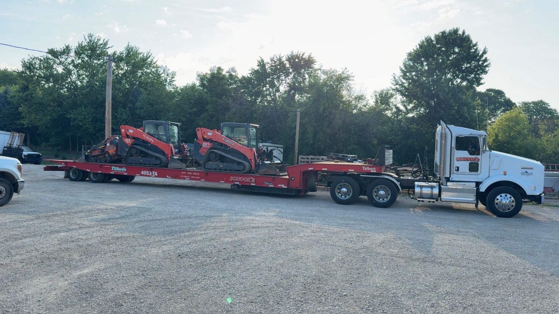 A semi truck is carrying a trailer with a tractor on it.