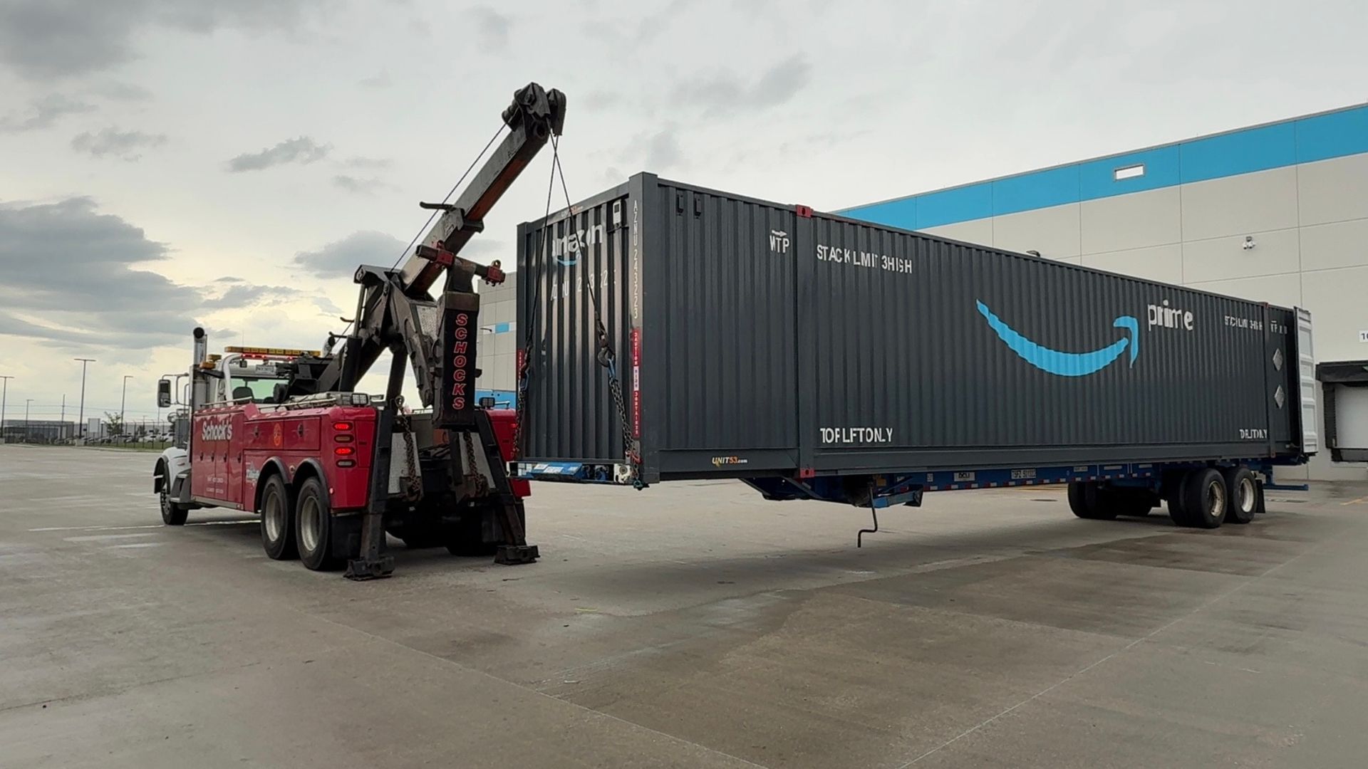 A tow truck is towing a large shipping container in a parking lot.