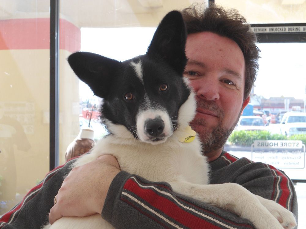 Man holding a black and white dog indoors, looking at the camera.