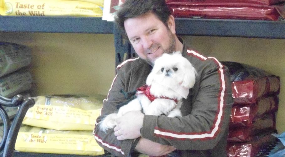 Man holding small white dog in a pet food store.