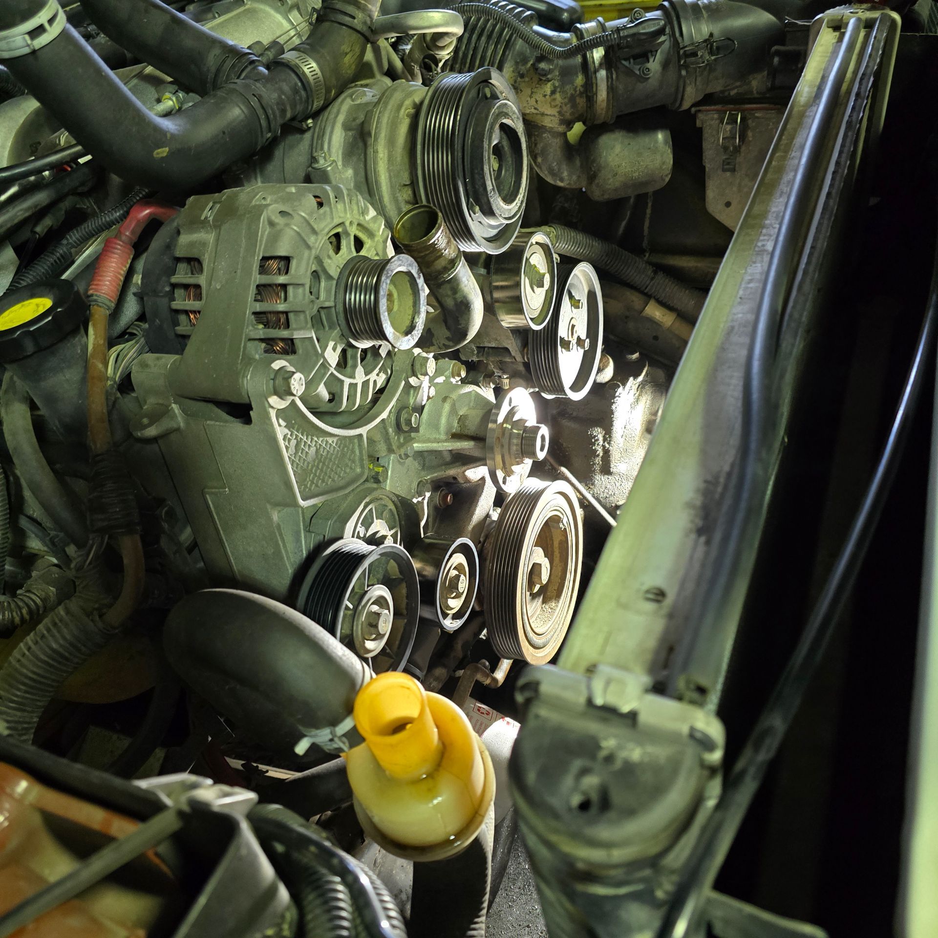 Engine bay with belts, pulleys, and alternator. Various tubes and components visible.