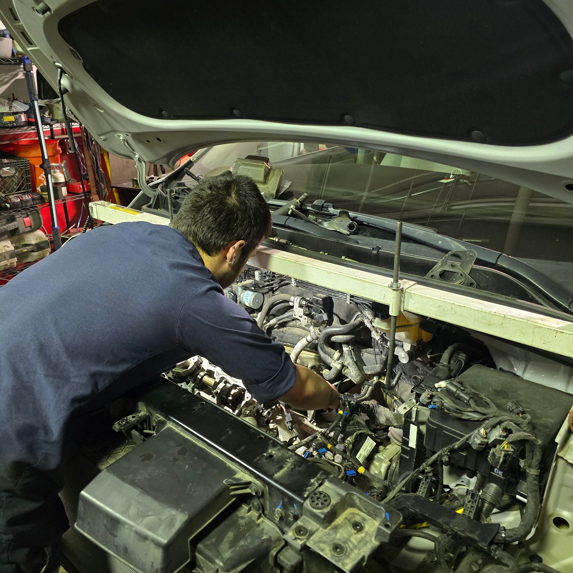 Mechanic working on a car engine under the hood in a well-lit garage.