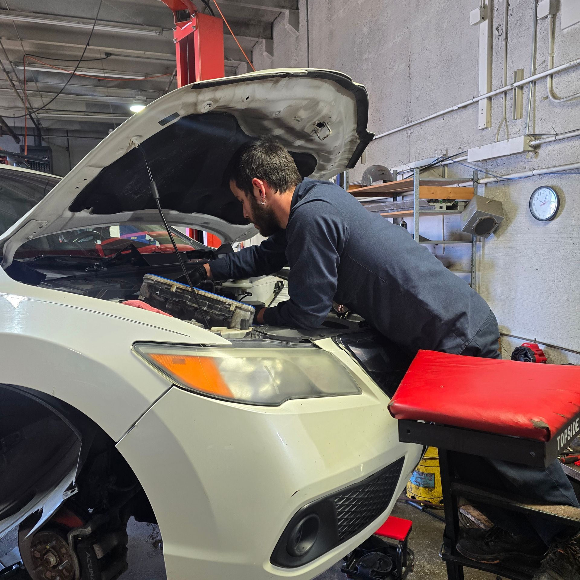 Mechanic working on a white car with the hood open in a garage.