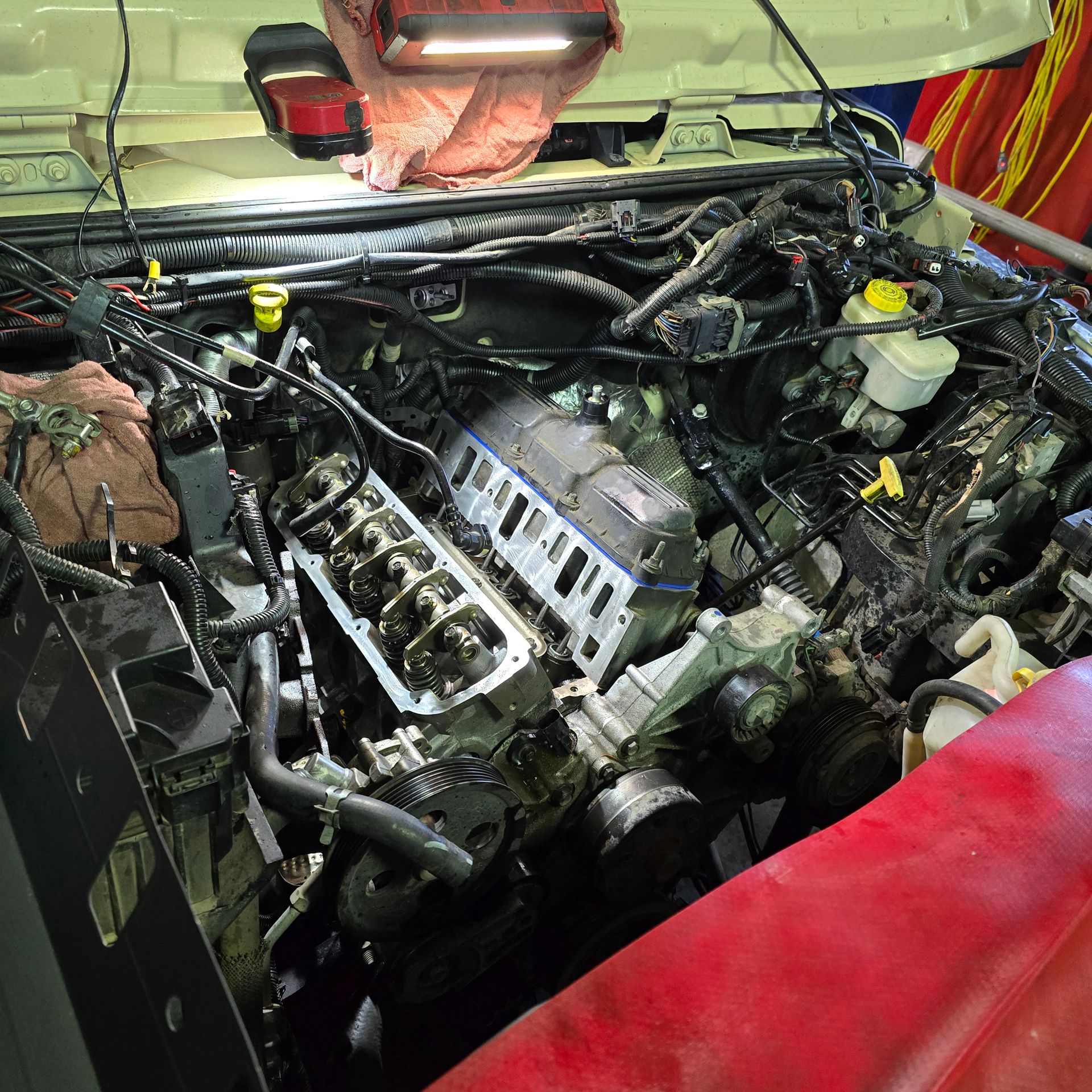 Engine of a vehicle with the valve covers removed and exposed, under a work light.